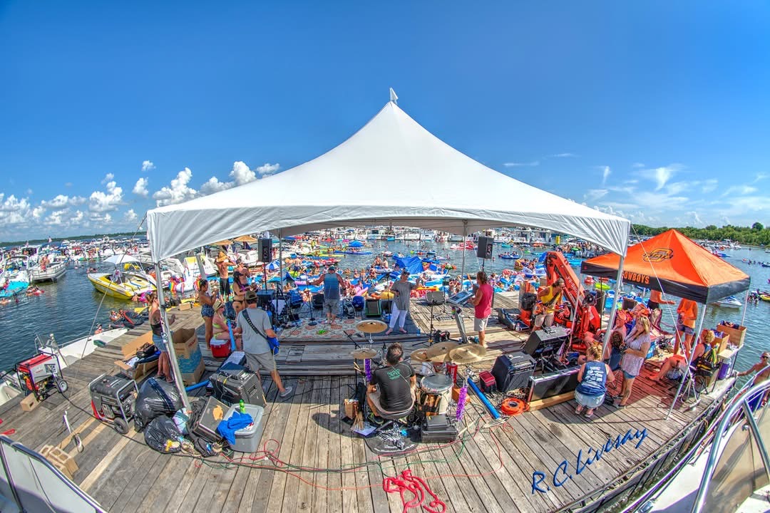 Live band performing on a floating stage under a white tent for boaters at Grand Lake Party Cove