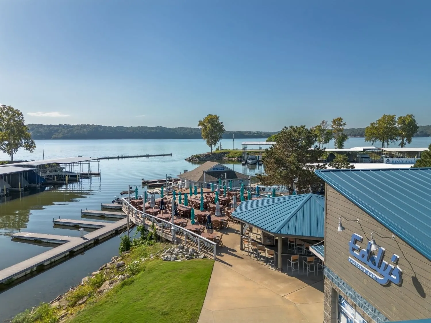 Aerial view of Eddy's Lakeside Bar waterfront patio with umbrellas and boat docks on Grand Lake at Shangri-La Resort